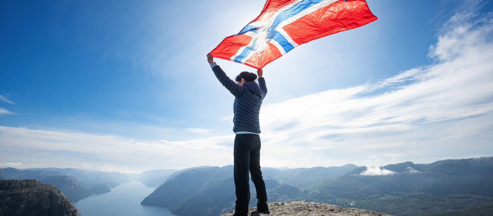 Frau mit einer wehenden norwegischen Flagge vor einem Naturhintergrund. © Andrei Armiagov - stock.adobe.com