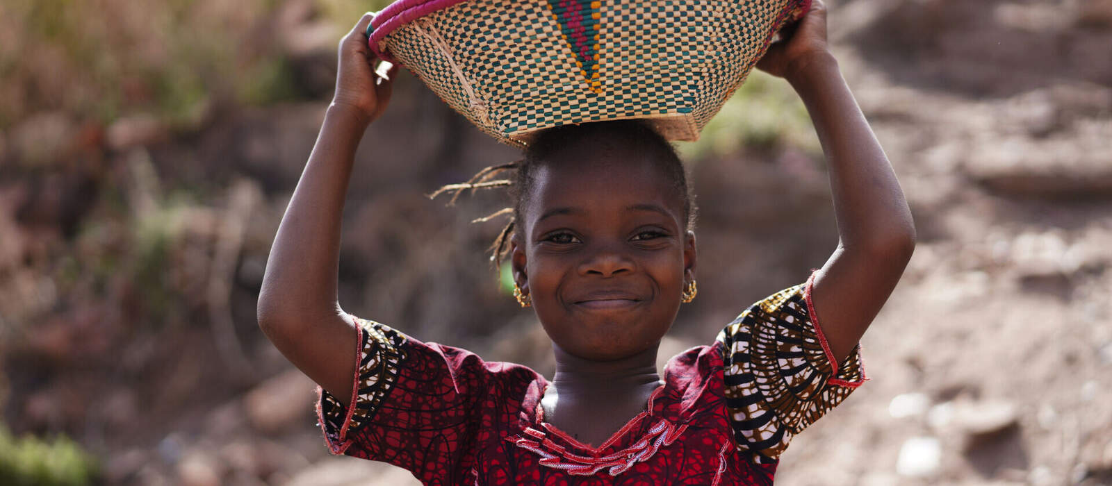 afrikanisches Mädchen mit offenem Lächeln und Korb auf dem Kopf © Riccardo Niels Mayer - stock.adobe.com